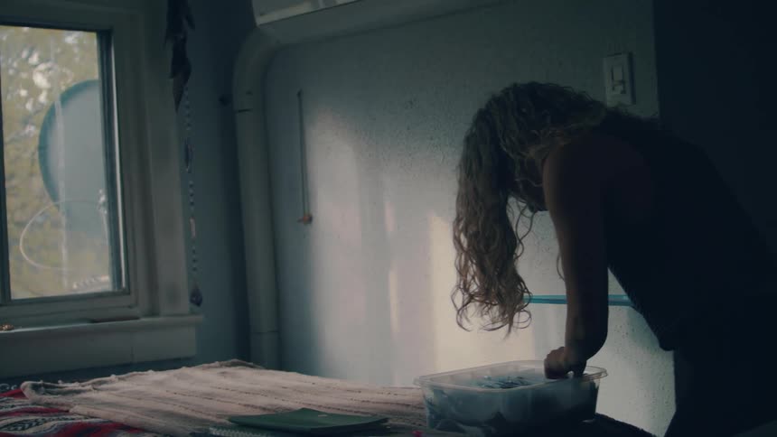 Blonde woman with curly hair takes out earrings from a plastic box in her room
