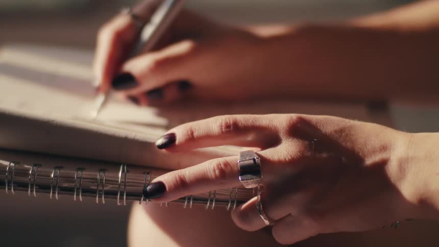 A female writing using a pen and a paper binder at a table