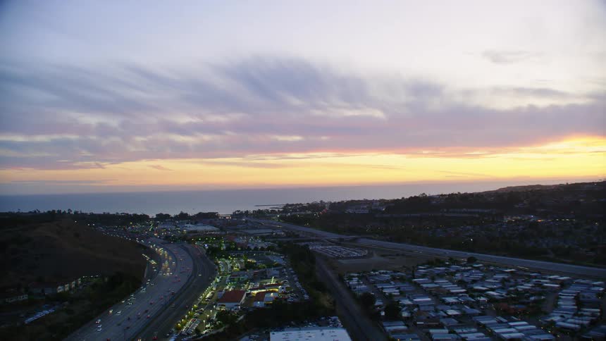 Yellows and oranges streak the horizon as heavy traffic passes along highway