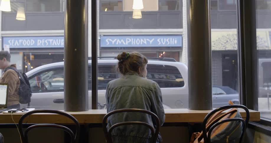 A woman is sitting in a restaurant facing towards a window