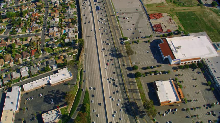 Cars travel on large city highways and streets past stores buildings and residential neighborhoods