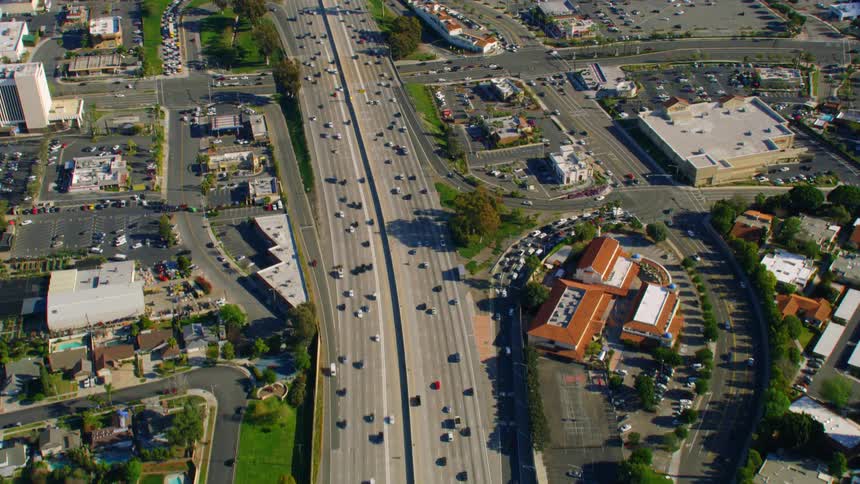 Traffic move on a large multi lane highway past stores office buildings and neighborhoods