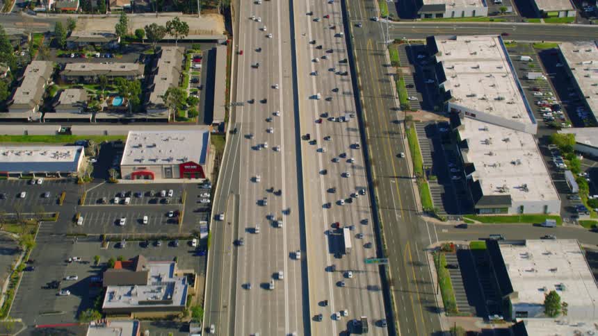 Cars and trucks travel on wide multi lane highways past offices and stores and neighborhoods