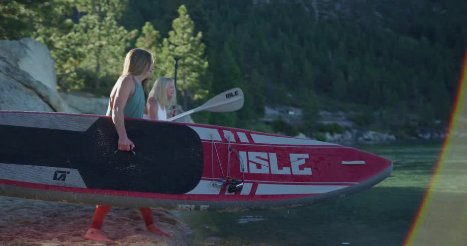 Young fit women carry rafts to the shoreline of a lake on the mountains in the morning