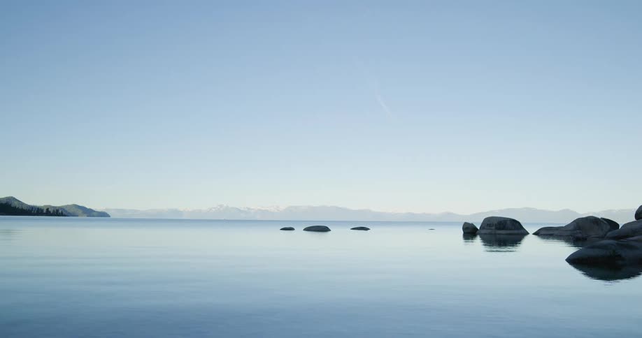 Large stones dotted throughout a vast lake under a clear daytime sky