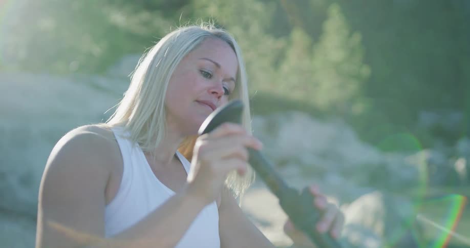 A woman by a lake adjusting the length of a paddle with trees rocks and water in the background