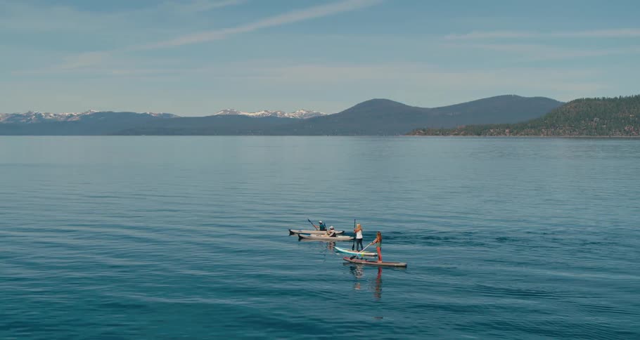 Two women paddle boarding in a lake as two people in canoes row past them
