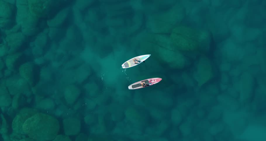 People standing paddle board across blue water through which lake bed is visible