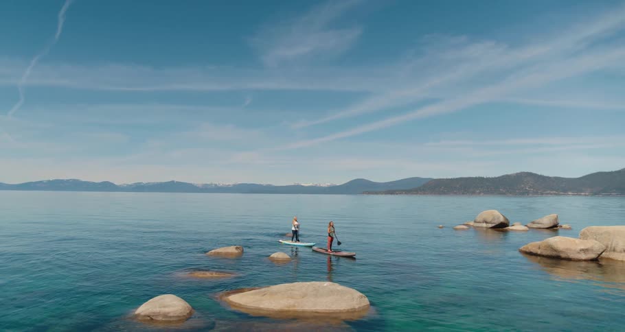 Two women paddle board on a mountain lake on a summer day