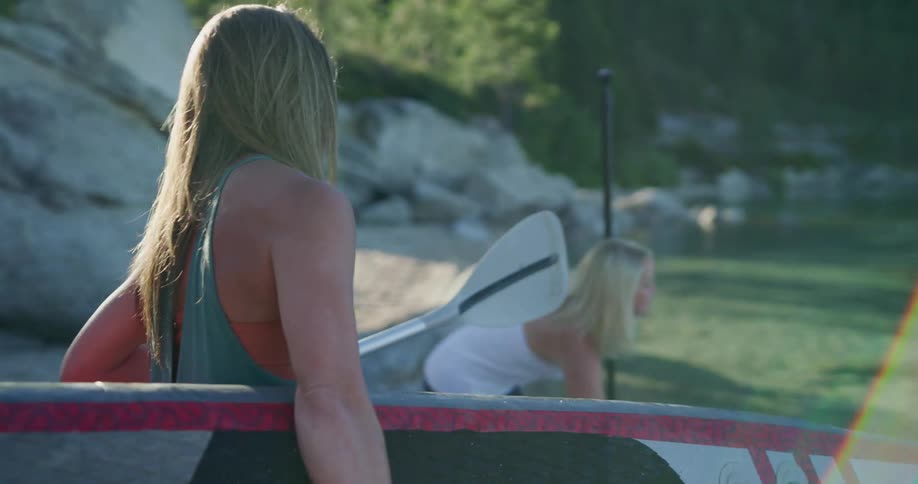 Two women putting their paddle boards into the river