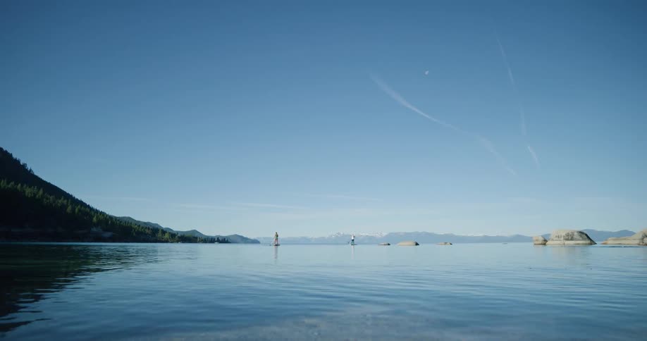 Two people surfboarding using paddles on a lake near the mountains