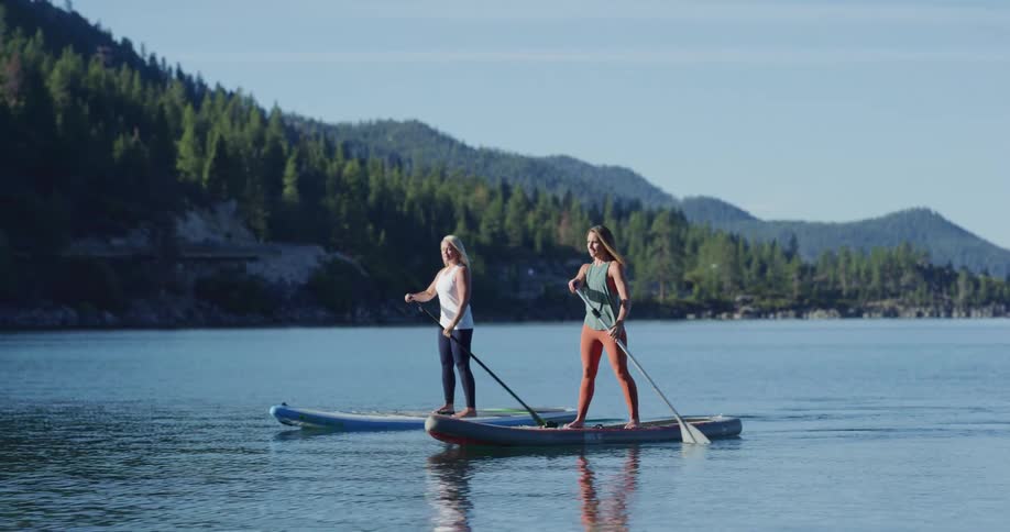 Two women standing in canoes and paddling in a lake