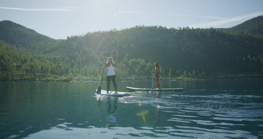 Two women paddle boarding on a lake in the sierras on a sunny day