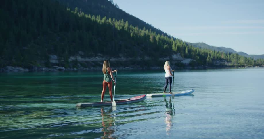 Two fit women rowing over surfboards on a lake in the mountains