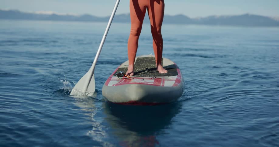 A woman stands on a paddle board and uses an oar to move along the lake
