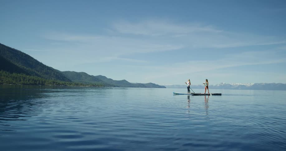 Two athletic women paddle boarding in a lake on the mountains