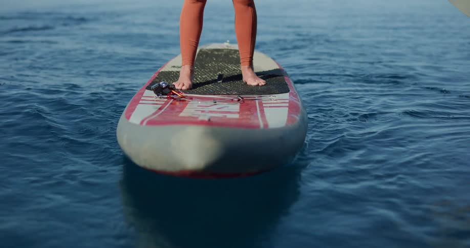 Woman with red tights stands on a paddleboard and moves in the lake against the blue sky