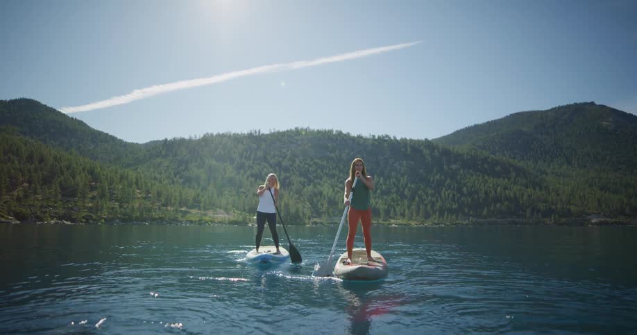 Two women paddle boarding on a lake in the sierras