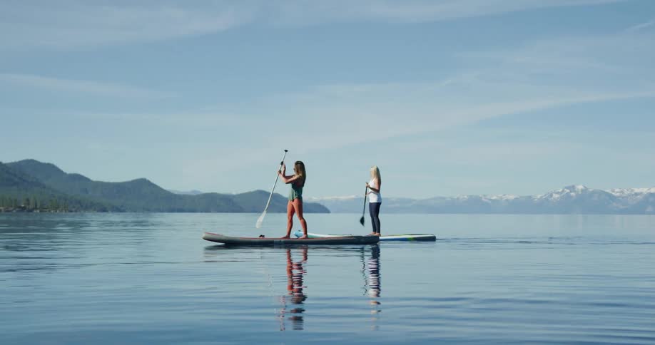 Two women paddle board across a mountain side lake