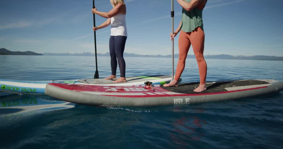 Two women standing on paddle boards paddle through a tranquil lake