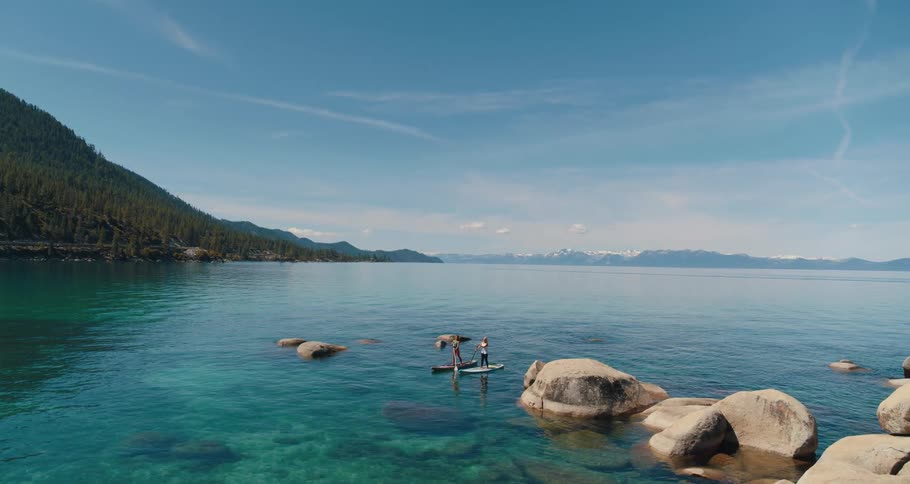 Aerial view of two fit women paddle boarding on the lake next to the mountains