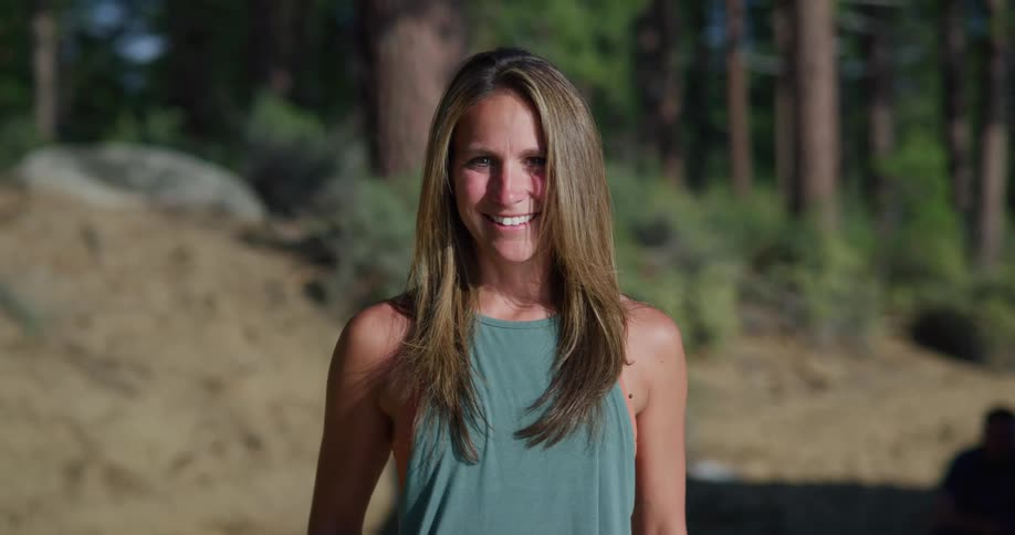 Woman with a blue strappy shirt brown hair smiles at the camera