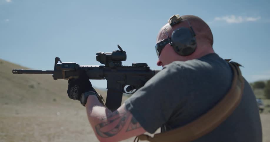 A man practices shooting a sniper rifle in a rural outside area