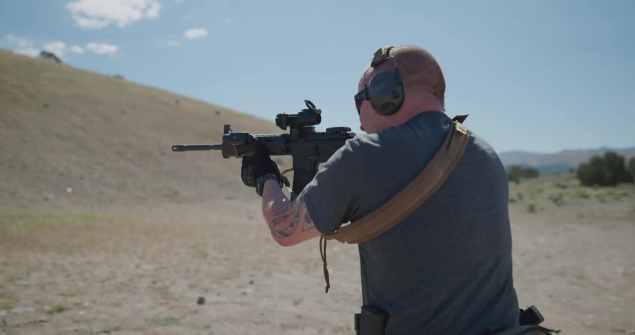 Man shooting an assault rifle in an outdoors shooting range near a hill