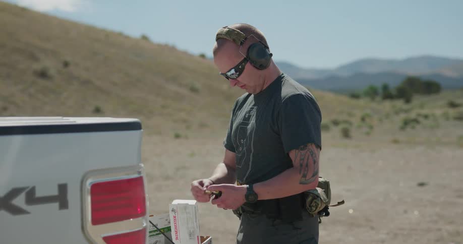A man stands at the rear of his truck and places bullets into a weapon