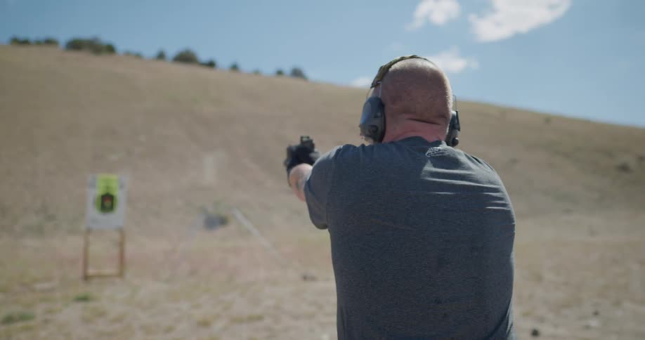 Man fires a gun at a target in front of a hill on a shooting range