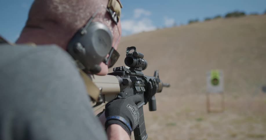 A man reloads a rifle before firing it at a shooting target in field on a sunny day