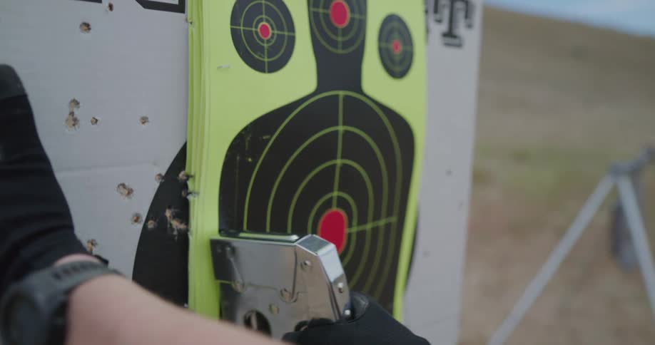 A person with gloves stapling a target on cardboard with the sky and clouds in the background