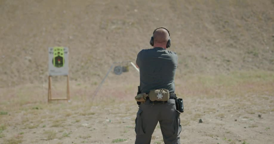A man draws a pistol and fires at a practice target while outdoors