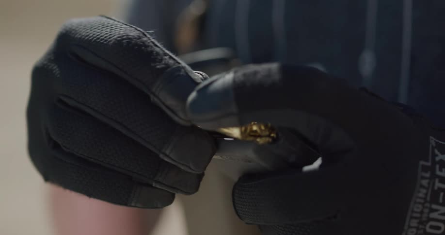 A man inserts bullets into a the magazine of a firearm while standing outdoors during the day