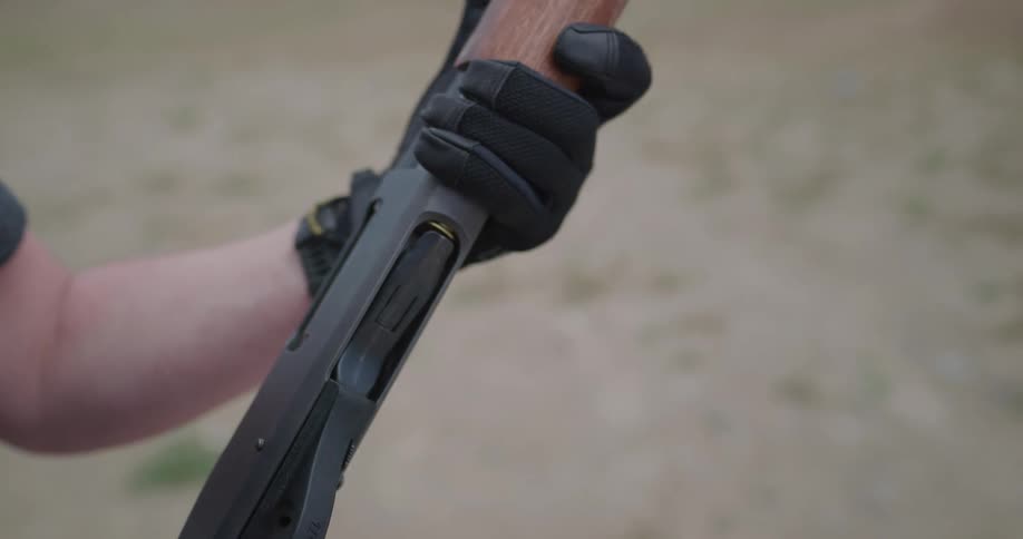 Man wearing gloves loads shells into a shotgun on a shooting range