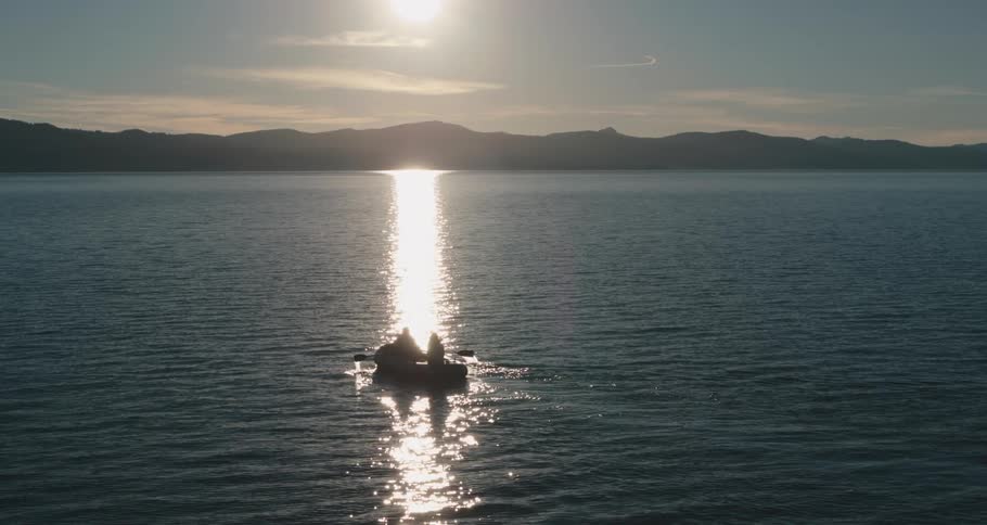 People row across rippling water reflecting sun on hay day