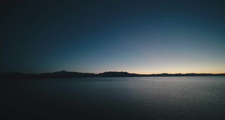 A calm ocean is dimly lit under a clear sky