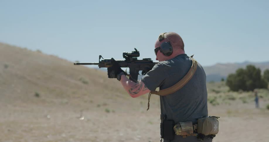 A man holds a rifle up and fires multiple rounds at a rural shooting range
