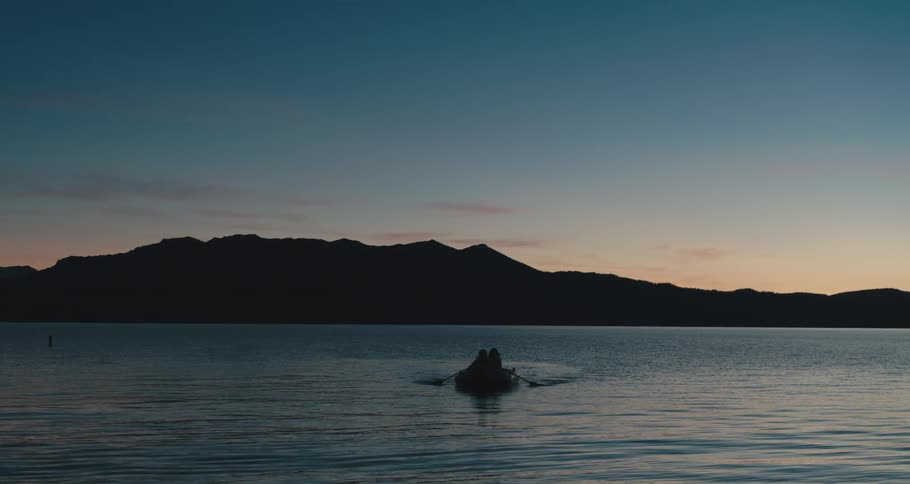 Two people rowing a boat in a lake with mountains in the distance