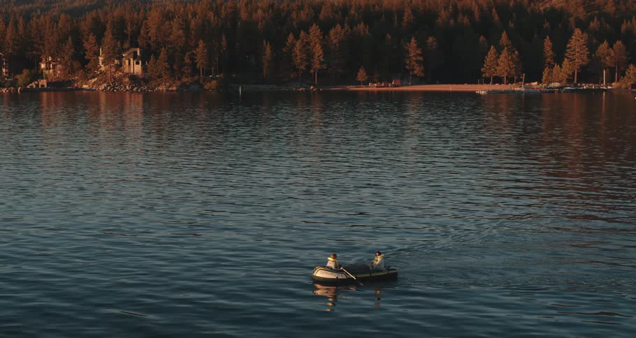 Two people sit in a dinghy on a lake as one person paddles