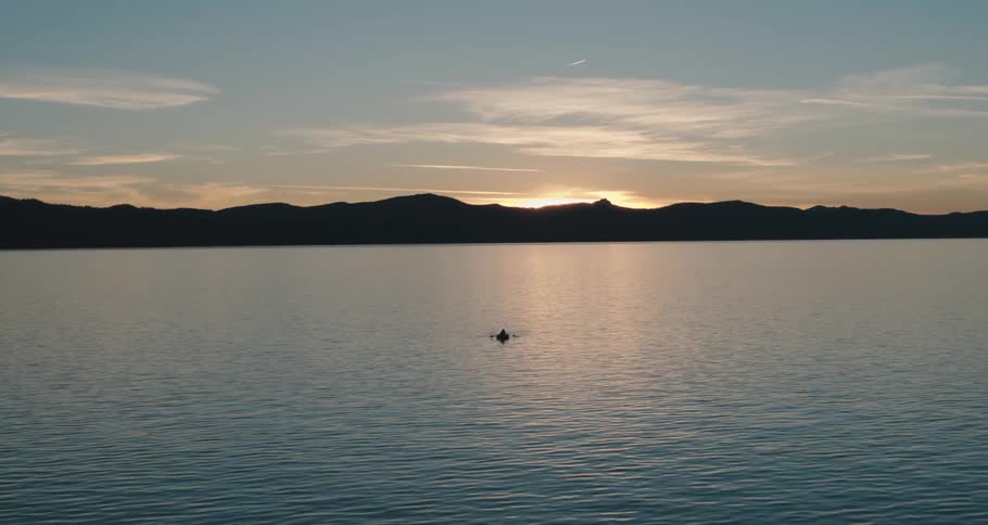 A raft with someone peddling on a lake with a mountain range the sky and clouds in the background