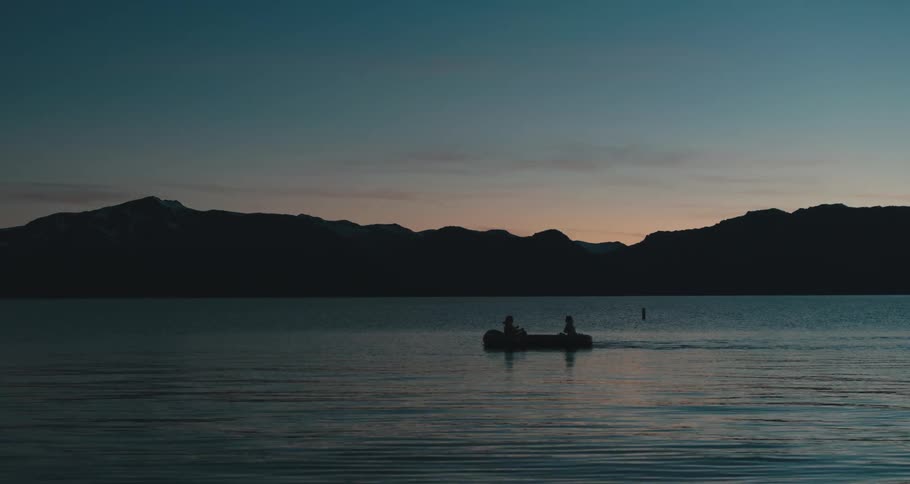Two people in a rowboat on a lake at dusk