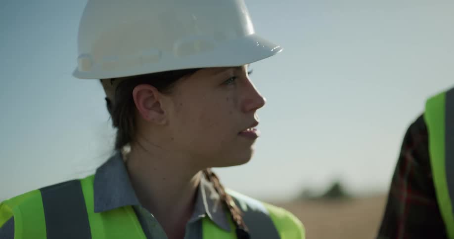 A woman in a hardhat nods as a coworker speaks to her at an outdoor site