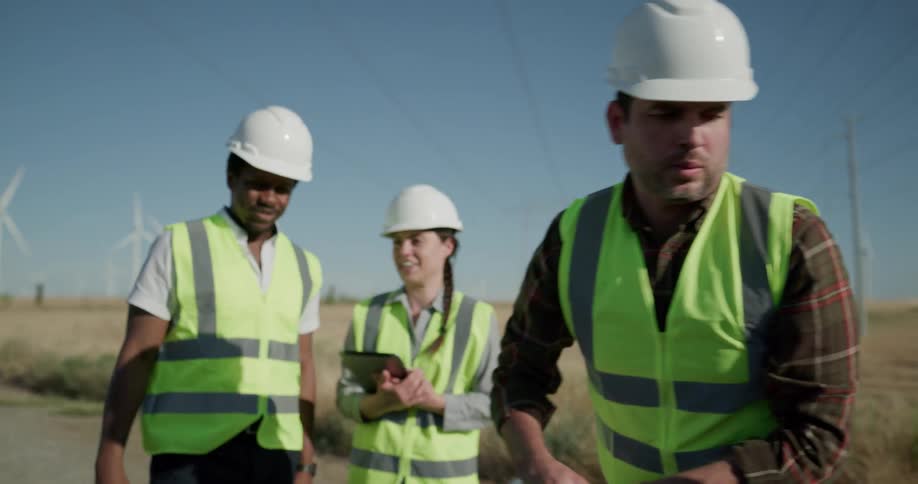 A man rolls up blueprints on on a wind farm as his coworkers stand and talk