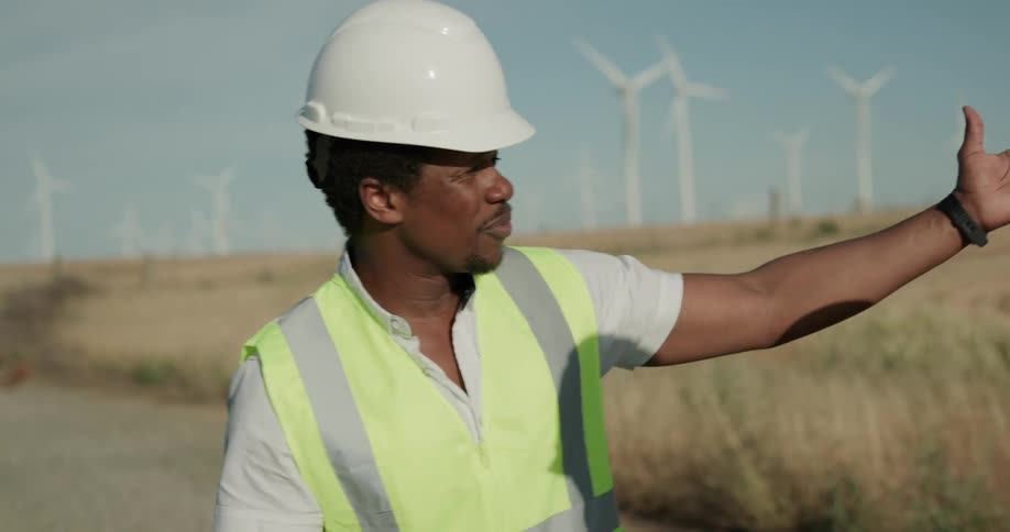 Two construction workers talk outside in a rural area by wind turbines