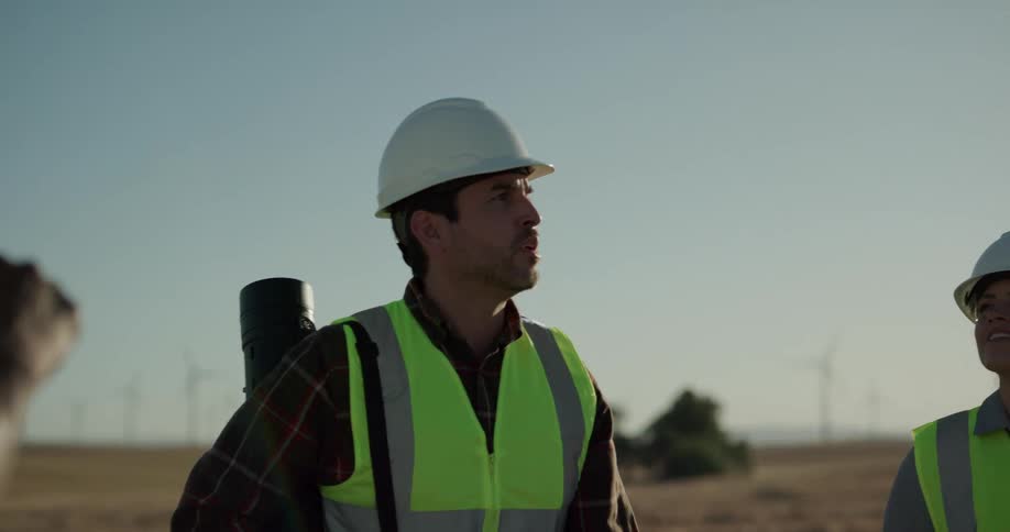 A group of workers stand outdoors among a field of wind turbines and speak as they study their surroundings