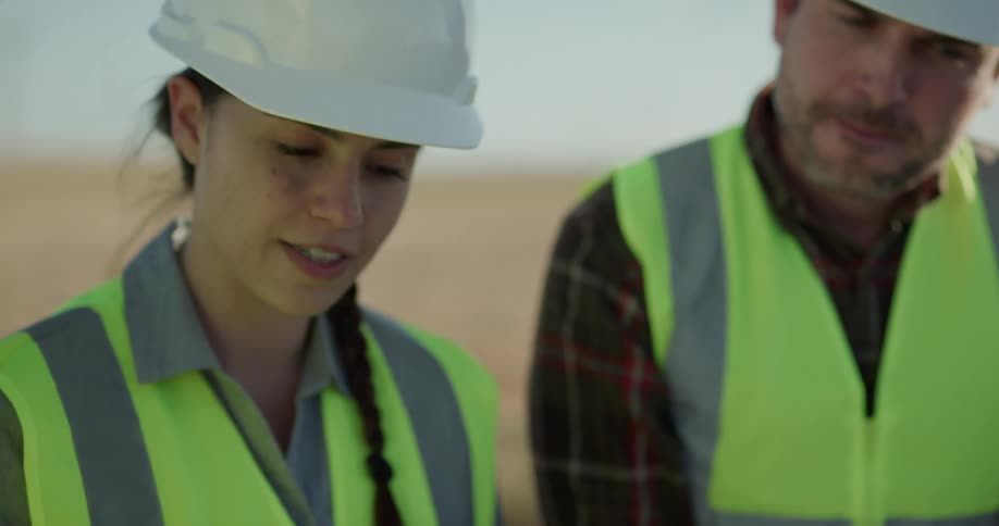 Two men and a women look at a tablet and blueprints