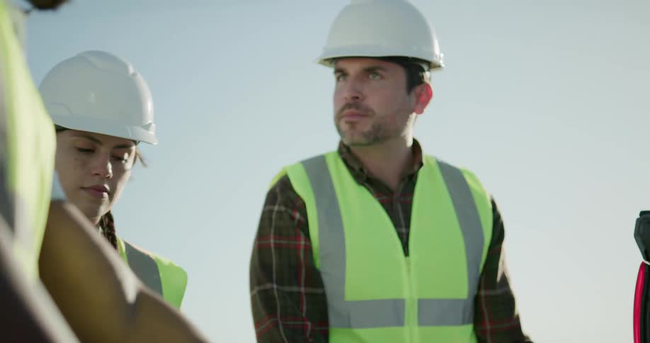 Group of construction workers check blueprints on the back of a truck in the field at sunset