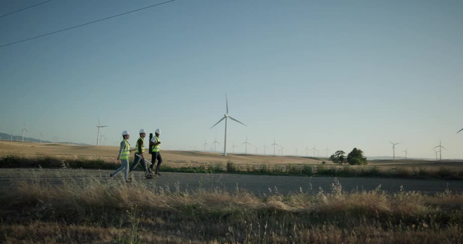 Three construction workers walking down a road near a field of windmills