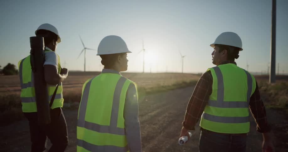Three construction workers walk down a gravel road running through a wind farm